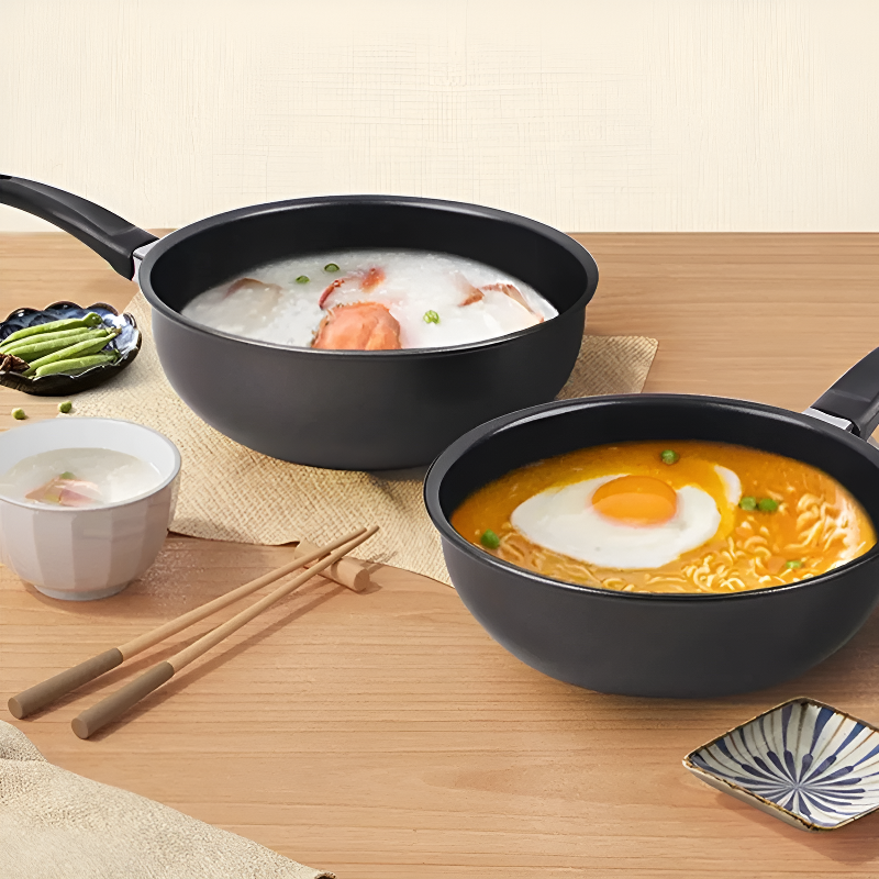 To woks på et træbord, den ene med risgrød, den anden med nudelsuppe og spejlæg, ved siden af spisepinde