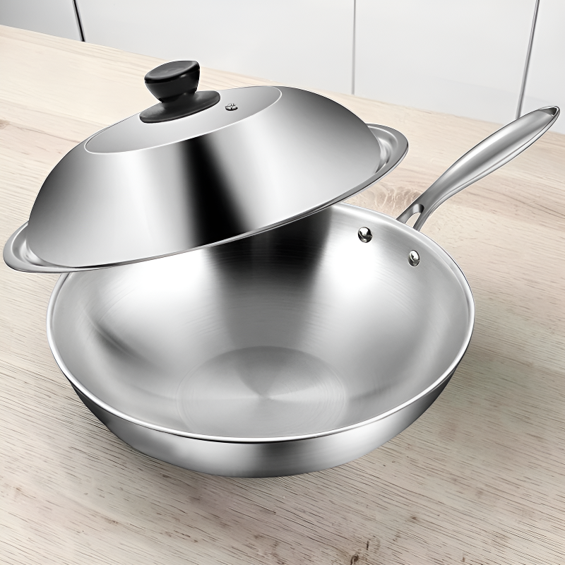 Wok i rustfrit stål med låget holdt skråt over kanten, på en lys træbordplade foran hvide skabe