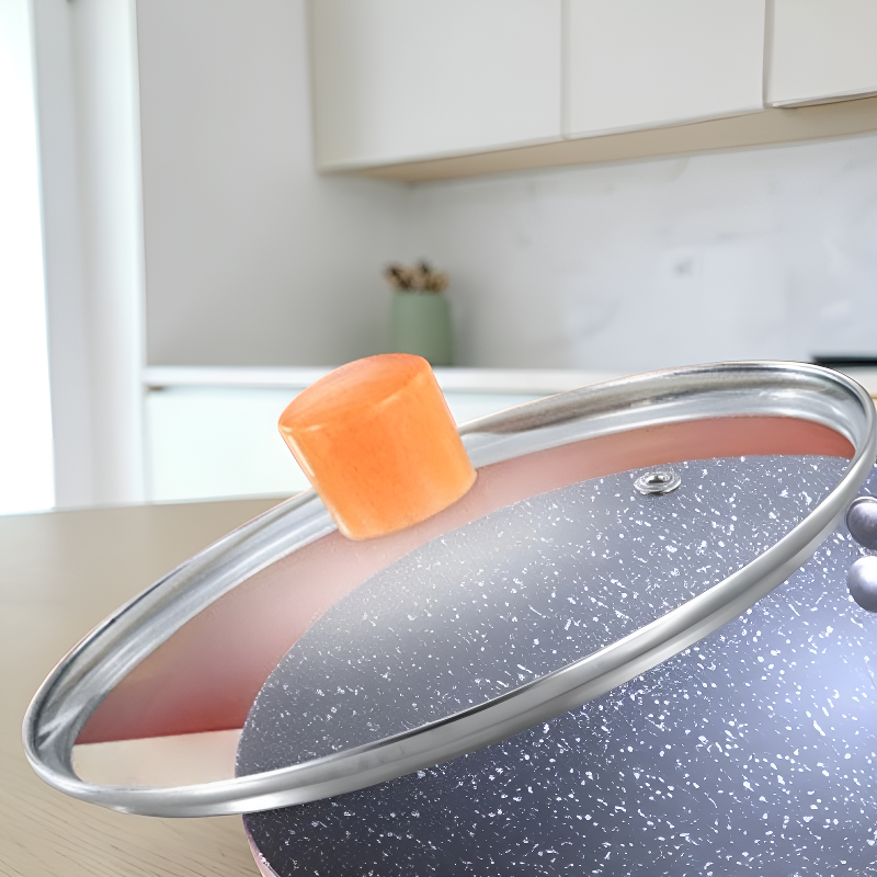 Nærbillede af glaslåget med metalkant og orange knop, lagt skråt over woken