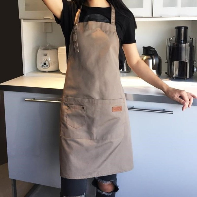 Kvinde i et køkken med det kaffebrune forklæde på, set forfra med halsrem og forlomme