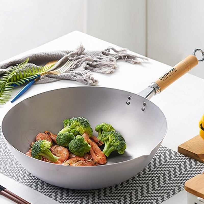Wok med rejer og broccoli på et bord med dækkeserviet, træskaftet peger mod højre
