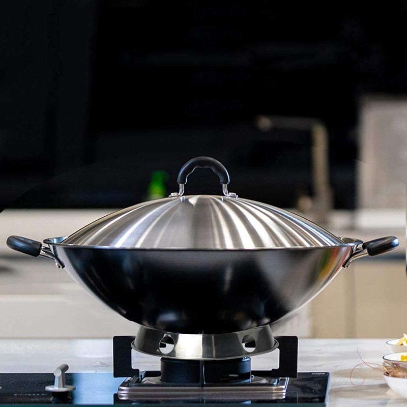 Blank wok med to sorte hanke, der står i ringen på et sort gaskomfur