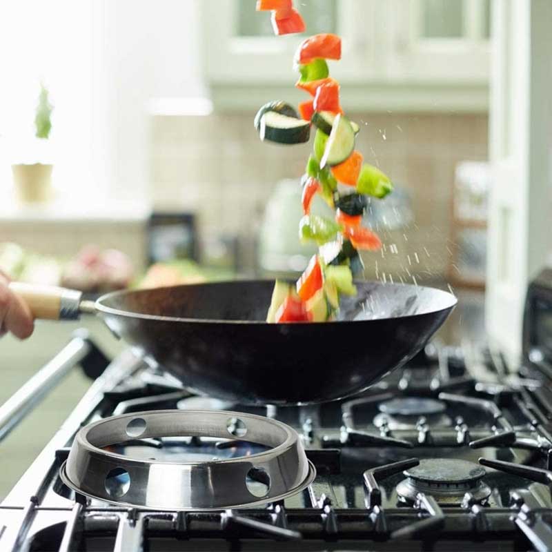 Tom wokring på risten af et gaskomfur, mens en hånd kaster grøntsager op i luften fra en sort wok