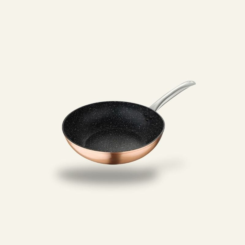 Le Monska wok set skråt fra oven med sort, prikket keramisk belægning indeni, kobberfarvet yderside og håndtag i metal