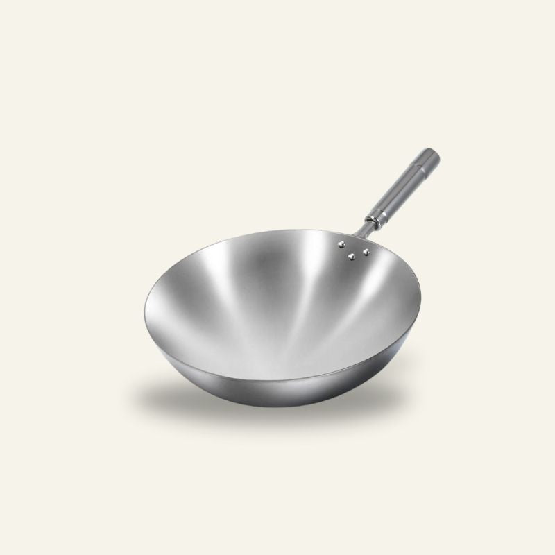 Le Pankaji wok i rustfrit stål med langt skaft i metal, set skråt ovenfra på en lys baggrund