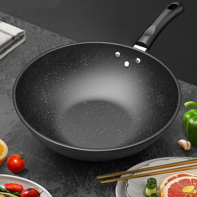 Tom wok set skråt ovenfra på et mørkt bord med grøn peberfrugt, tomater og spisepinde omkring