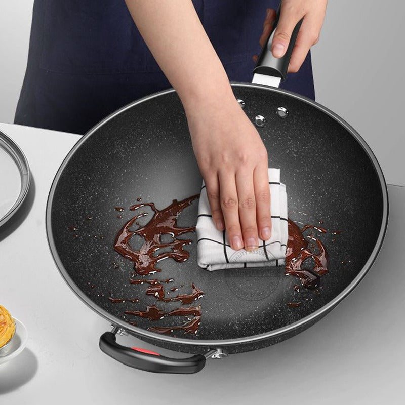 En hånd tørrer brun sauce op fra bunden af woken med et viskestykke, mens den anden holder skaftet