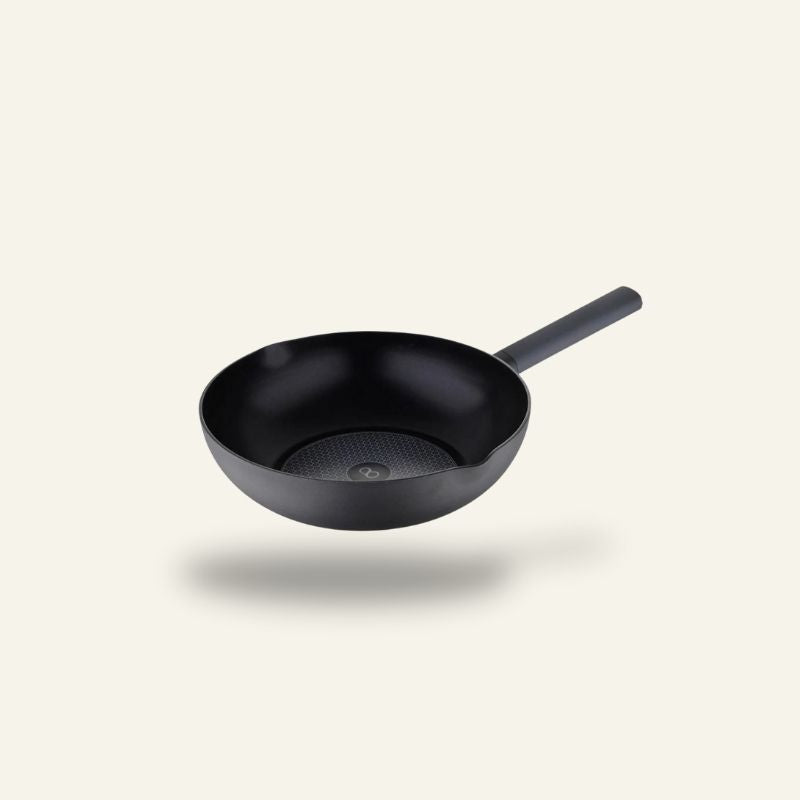 Le Caska wok i sort med flad bund og langt skaft, set skråt ovenfra på lys baggrund